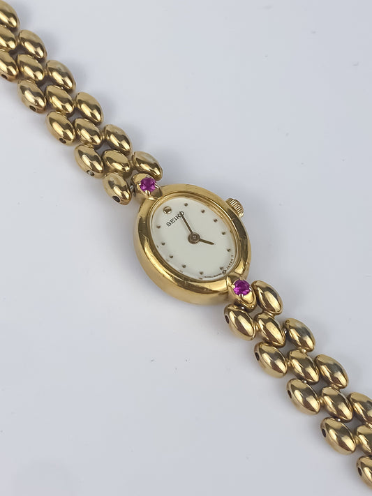 Gold wristwatch with a white face and chain link strap on a light gray background